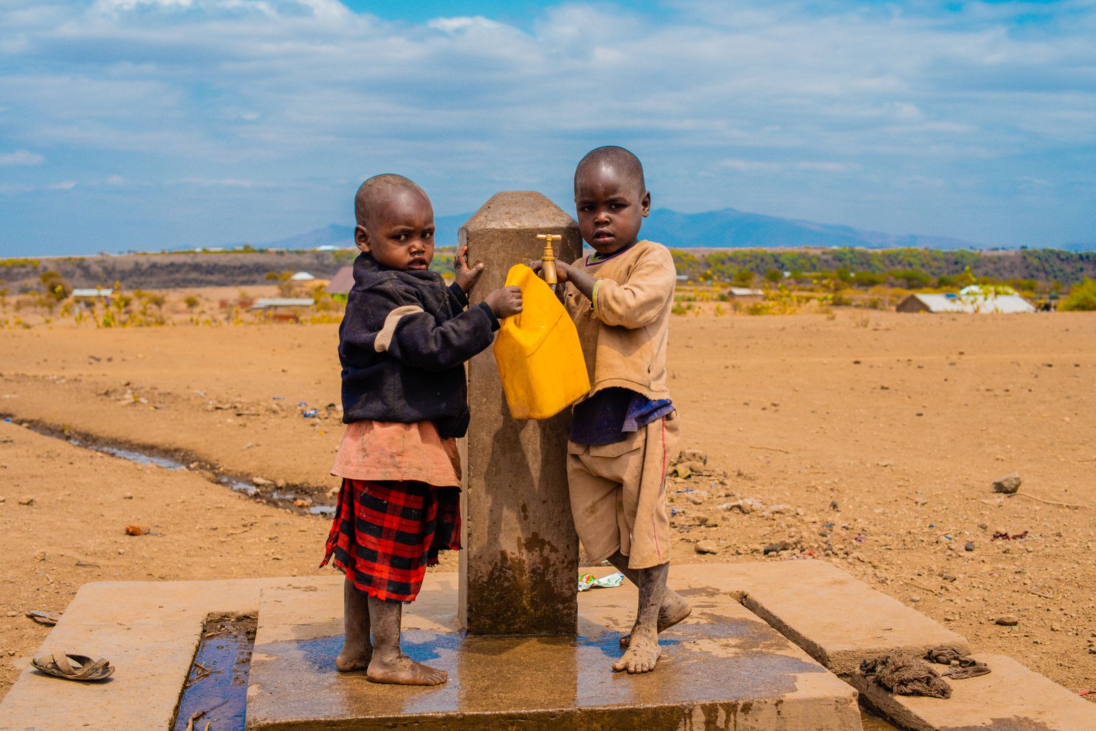 Two children filling a water container at a borehole tap